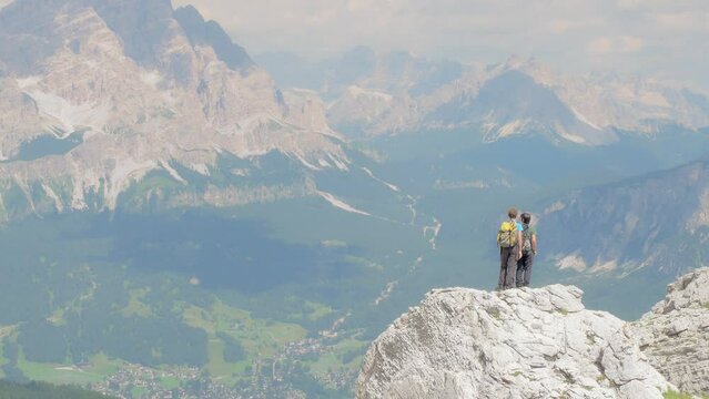 two young friends admire the horizon from the top of a rock. they are equipped with rucksacks and sports clothes because they are exploring the dolomites chain in a sunny summer day