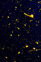 closeup of yellow paint drops on blue paper background