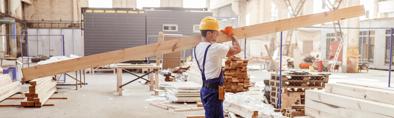 Male builder carrying wooden plank at construction site