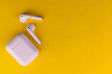 Modern wireless bluetooth headphones with a charging case on a yellow background.Copy space.