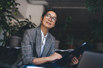 Attractive female entrepreneur in optical spectacles pondering on informative notes - analyzing...
