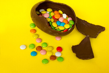 A cracked chocolate Easter egg with colorful little round candies inside. Happy Easter. Chocolate. Sweets for children and adults. Candy. Dessert. Copy space. Top view. Flat lay