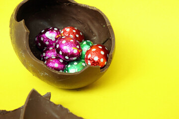 A cracked chocolate Easter egg with colorful little round candies inside. Happy Easter. Chocolate. Sweets for children and adults. Candy. Dessert. Copy space. Top view. Flat lay
