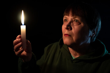 An elderly woman in the dark holds a candle in her hands.