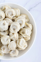 Russian meat dumplings on a white plate, top view, close-up. Dumplings with meat filling on a white, marble background.