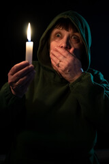 An elderly woman in the dark holds a candle in her hands.