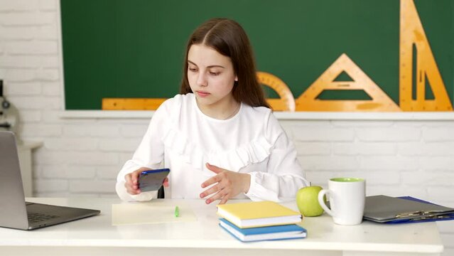 Serious kid doing classwork using mobile phone in classroom, smartphone learning