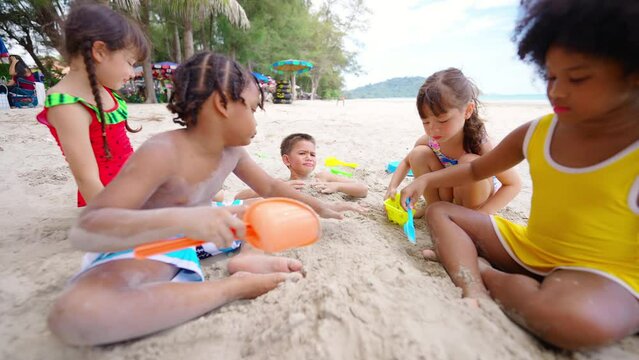 Group of Diversity little child boy and girl friends sitting on the beach playing sand with beach toy together on summer vacation. Happy children kid enjoy and fun outdoor lifestyle on beach holiday
