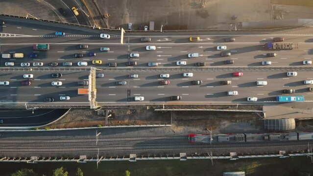 Top view to a busy Moscow highway with heavy traffic on a sunny summer evening. Camera moving above the road showing colorful cars, trucks and a train passing along the railroad.