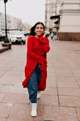 Full-lenhgt portrait of stylish pretty woman with dark hair and great smile is wearing long red knitted coat.