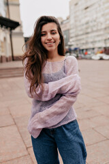 Obraz premium Romantic lovely woman with long wavy dark hair is wearing tender spring thin sweater is posing at camera and smiling 