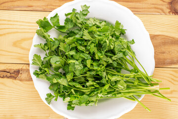 One bunch of fresh green parsley with a white ceramic plate on a wooden table, macro, top view.