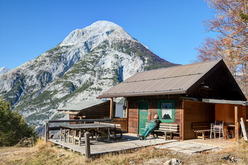 A mountain hiker enjoys the midday sun on a lonely, dilapidated mountain hut against the impressive...