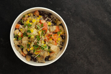 Healthy bowl with wild rice, chicken and vegetables on dark background. Food delivery service and daily ration concept.