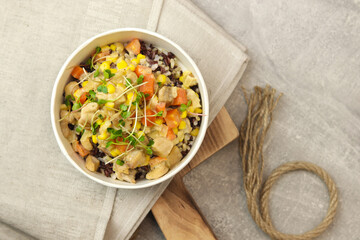 Healthy bowl with wild rice, chicken and vegetables on wooden board on gray background. Food delivery service and daily ration concept.