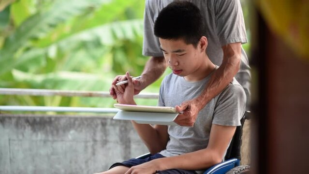 Young man with a disability and parent help train him to use a pen for writing on laptop screen for learning, remote education or social media, He had a tremor caused by Cerebral palsy, or CP, Ataxia.