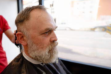 Barber trimming and cutting bearded man with shaving machine in barbershop. Hairstyling process.