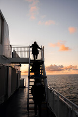Beautiful sunset sky on ferry boat with anonymous passengers climbing steps up ladder to top deck...