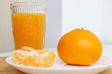 Glass of natural Mandarin orange juice in focus in the background, a full round orange and peeled orange pieces on a dish out of focus in foreground, selective focus used