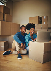 We dont have much yet but we will. Shot of a cheerful young couple browsing on a laptop together while being surrounded by cardboard boxes inside at home.