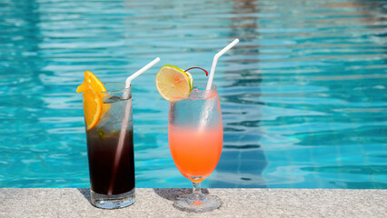 Drink tropical cocktail on vacation. Glasses with iced alcoholic cocktails near blue swimming pool in modern hotel resort. Fruit cocktails decorated with slices of orange and lime. Weekend in Thailand