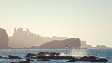 Windsurfer at sunny windy day against the backdrop of coastal cliffs and old castle on the coast. Tantallon Castle, Scotland 
