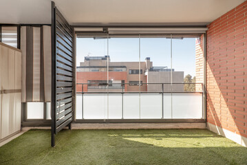 Terrace with glass wall, artificial grass floors and painted iron railing in an urban residential house