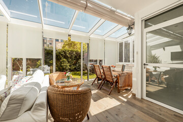 Terrace with access to a garden with aluminum and glass carpentry with large sliding doors with white extensible shutters, and wicker wood furniture and a large white sofa