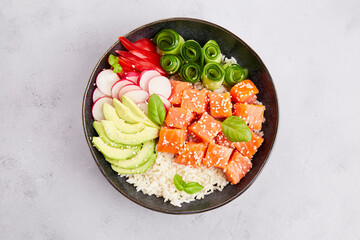 Poke bowl with salmon tuna, rice, avocado, cucumber, radish, pepper, sesame seeds on grey...