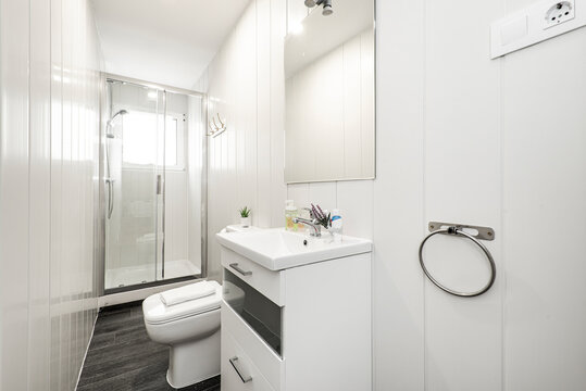 Bathroom with white resin sink, white wood furniture, shower cabin with glass partition, square frameless mirror and white woodwork