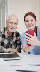 A young woman takes a selfie with her retired father. They pose and smile