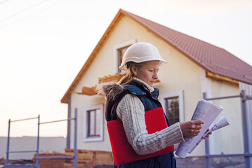 Young female construction specialist reviewing blueprints at construction site