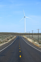 Road in Central Washington State into the distance with a wind turbine with a dotted yellow line and blue sky