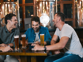Time to talk business over a beer. Shot of three cheerful young men drinking beer together at a table inside of a beer brewery during the day.
