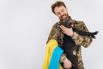 Fototapeta premium Ukrainian soldier in military uniform with a yellow and blue flag holds a dog in his arms on a white background