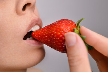 Beautiful young woman with strawberry in mouth, closeup. Woman's mouth eating strawberries. Concept of a healthy lifestyle with organic products and vitamins. Beautiful female lips with strawberries