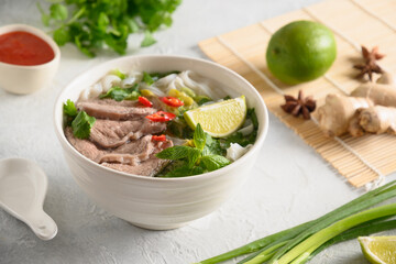 Pho Bo Soup with beef, rice noodles, ginger, lime, chili pepper in bowl on white background. Close up. Vietnamese and Asian cuisine.