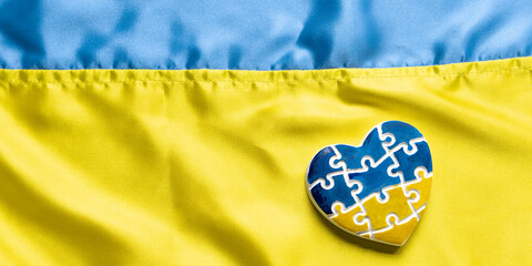 Heart in the form of puzzles with the colors of the flag of Ukraine on a blue-yellow canvas. Support Ukraine