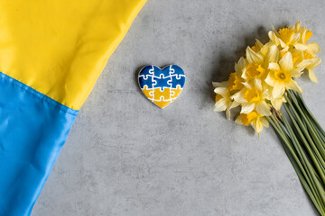 Heart in the colors of the flag of Ukraine on a gray background with yellow flowers