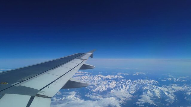 Airplane flight. Wing of an airplane flying above the snow mountain. View from the window of the plane. Aircraft. Traveling by air. 4K UHD video
