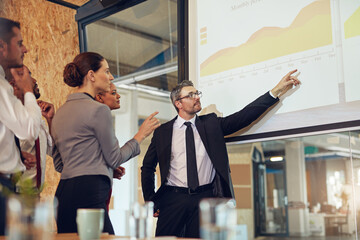 Running through the numbers with his team. Shot of an executive giving a presentation on a projection screen to a group of colleagues in a boardroom.