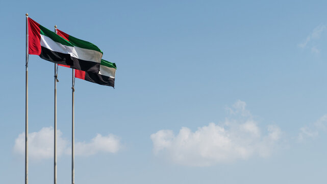 United Arab Emirates UAE flags waving against blue sky with copy space.
