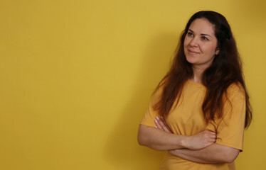 Obraz premium Beautiful woman in yellow t-shirt with long dark hair on yellow paper background. Pleasant brunette on a yellow background.