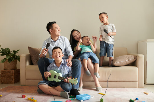 Happy Asian family of five laughing, playing ukulele and singing song into microphone
