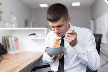 attractive young man in the office eating instant noodles