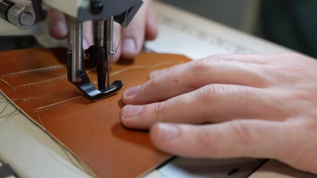A woman sews leather on a sewing machine and makes leather embroidery. Seams and threads