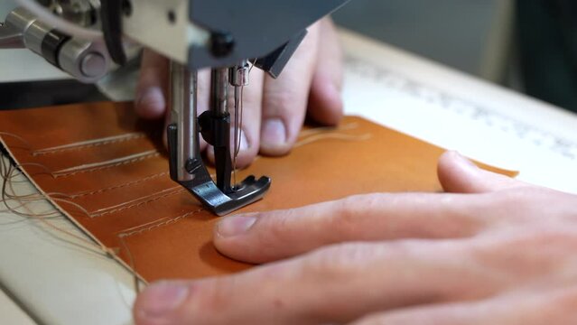 A woman sews leather on a sewing machine and makes leather embroidery. Seams and threads