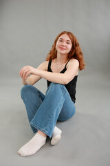 beautiful young girl model redhead. model in jeans and black top on a gray background. studio shooting. model with red hair and unusual appearance.