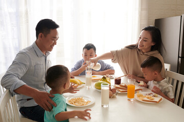 Smiling woman pouring milk for husband and sons at breakfast table