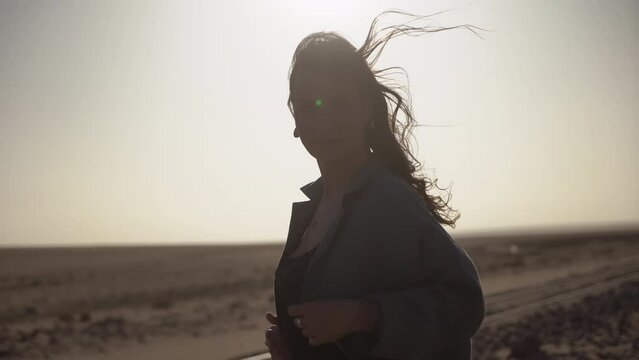 Silhouette of young woman in desert. Girl on railroad track in strong wind.